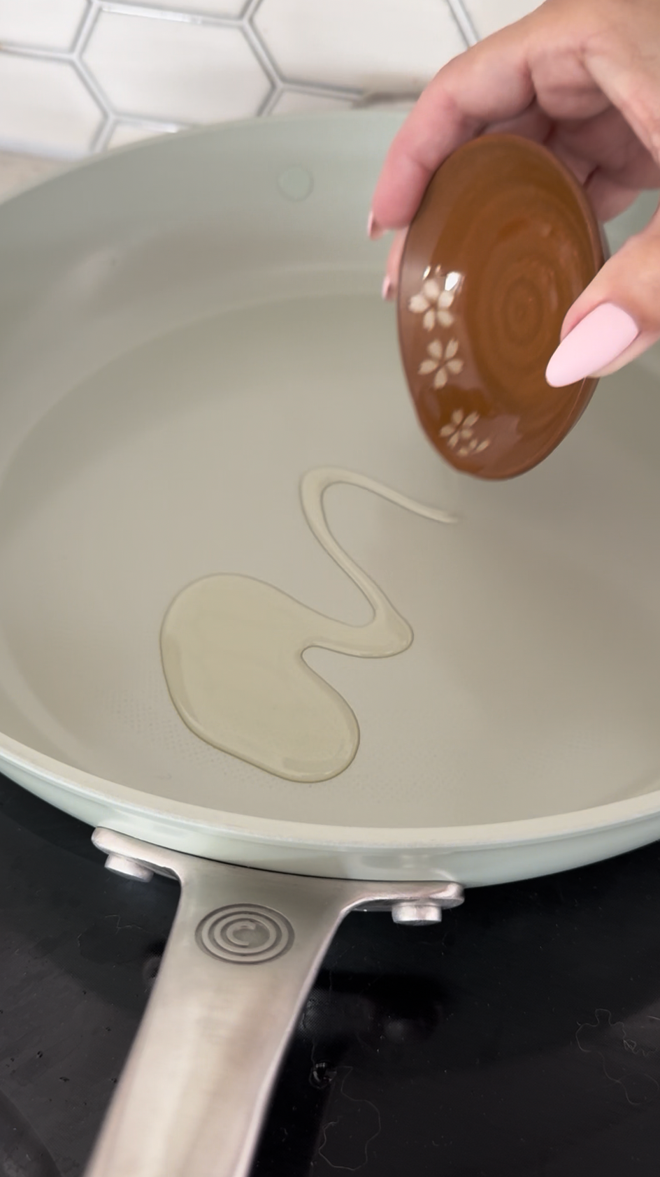 Oil being poured onto sage green ceramic frying pan