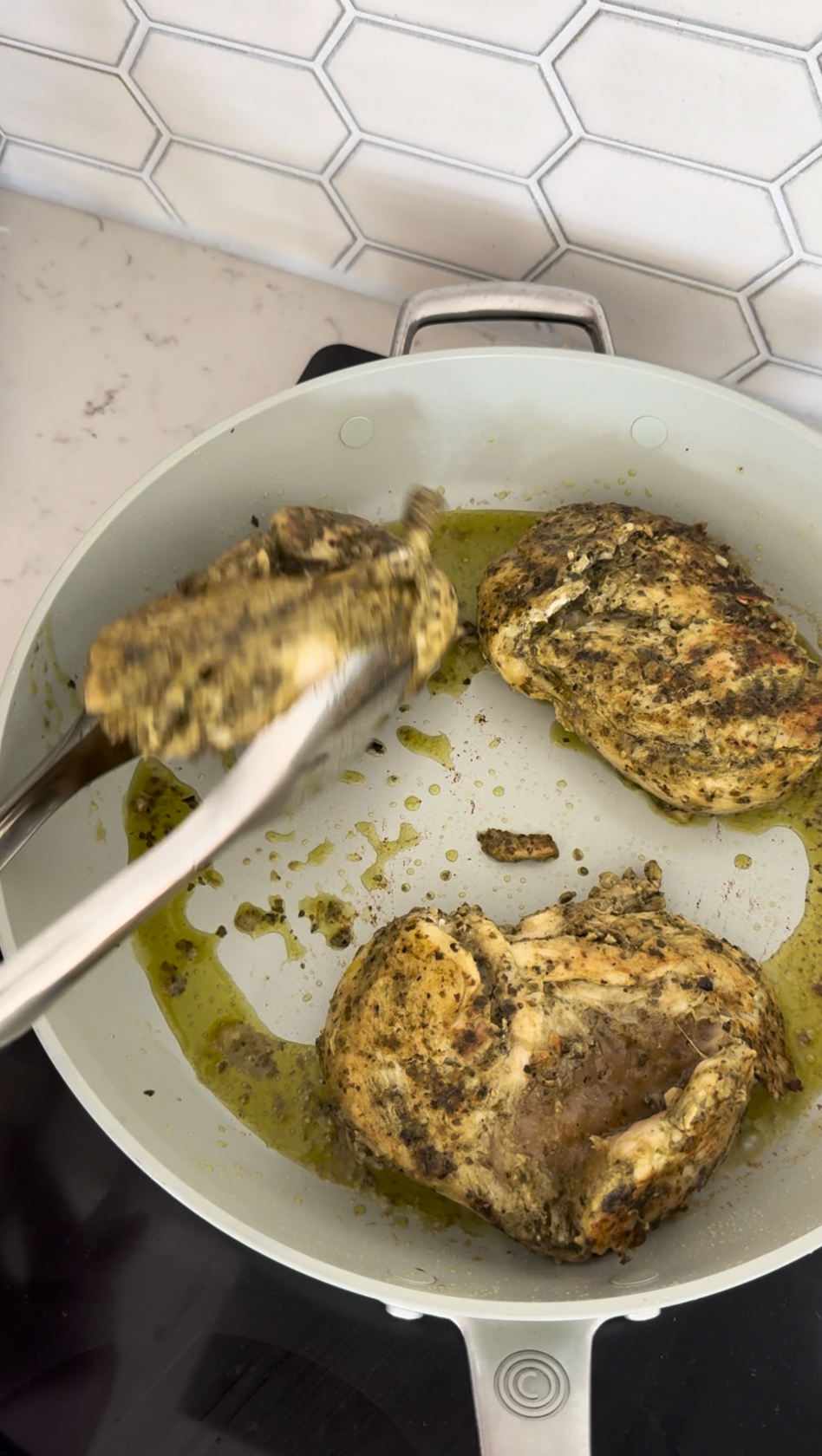 Seasoned chicken being turned over by tongs in a ceramic saute pan