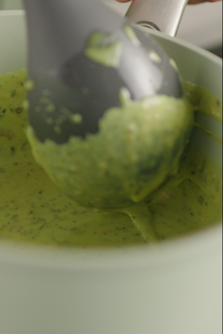 Ladle stirring a green sauce in a ceramic pot