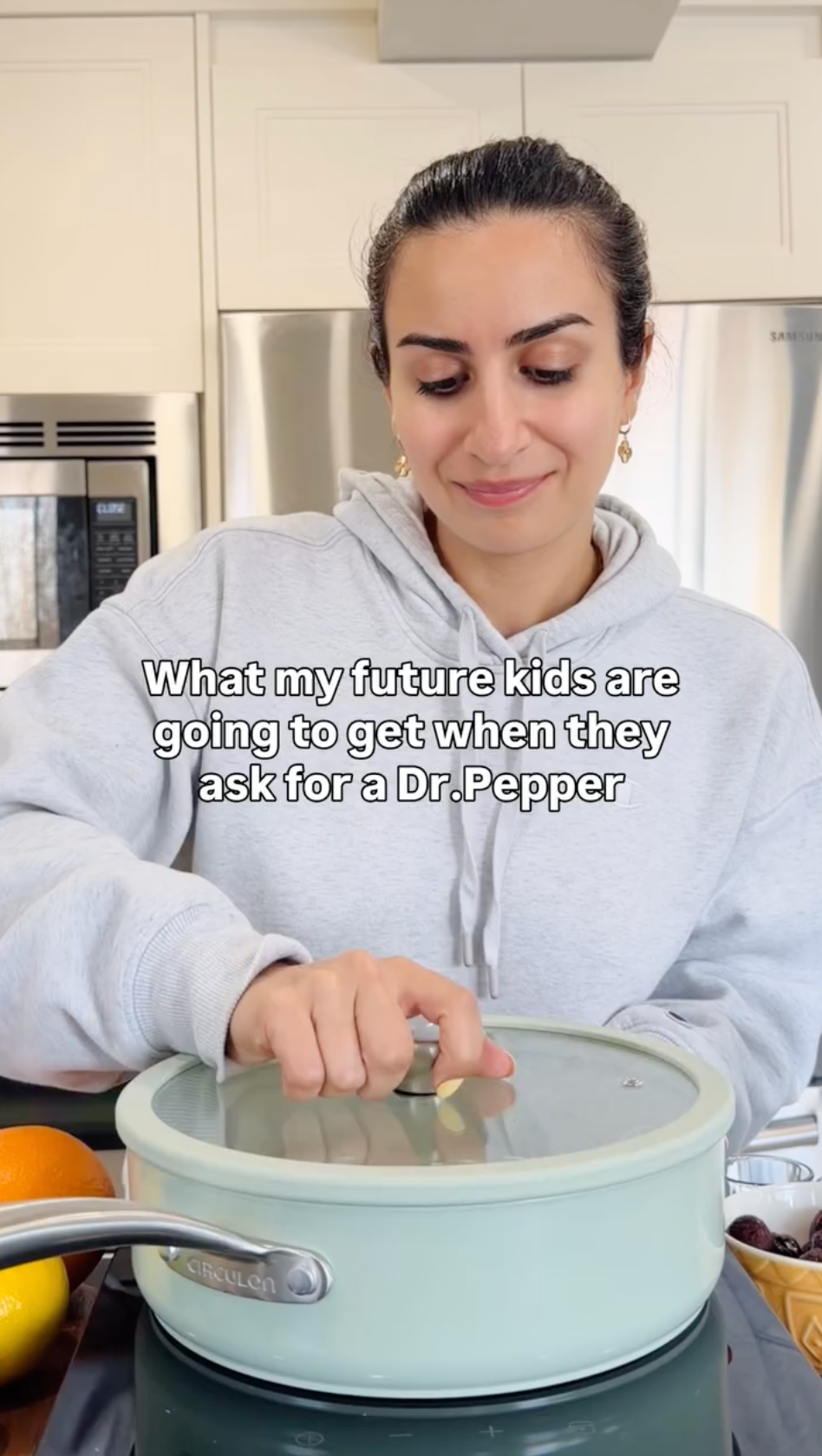 A woman in gray hoodie grabbing knob on lid of ceramic saute pan