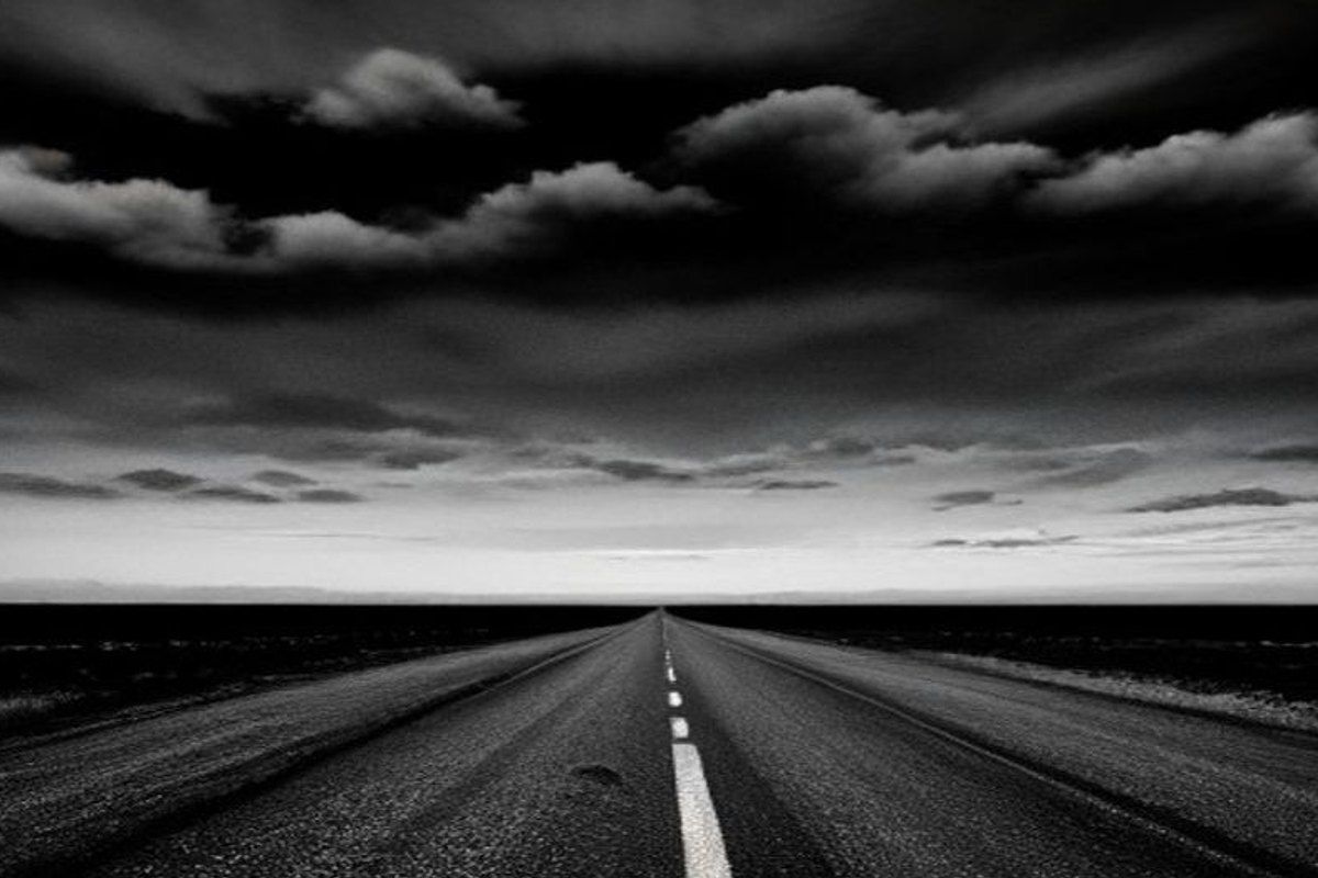 Ruta americana vacía con autos abandonados al costado y cielo amenazante, desolación postapocalíptica