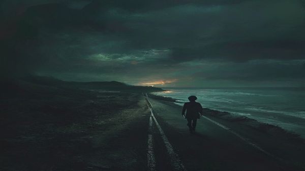 Un niño camina por una carretera costera desolada al atardecer, con un reino de fantasía medieval brillando en el horizonte entre dos mundos