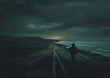 Un niño camina por una carretera costera desolada al atardecer, con un reino de fantasía medieval brillando en el horizonte entre dos mundos