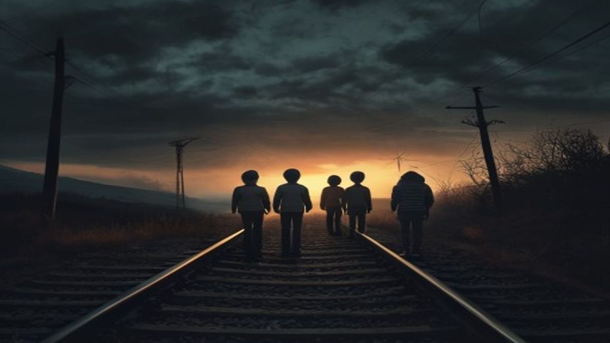 Un grupo de chicos parados juntos sobre las vías del tren al atardecer, frente a un horizonte oscuro y amenazante