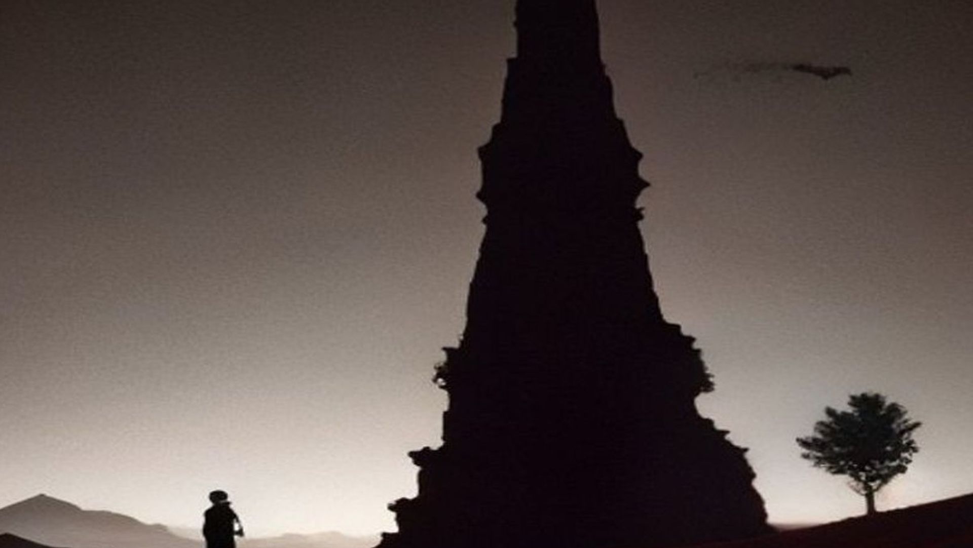Cinco viajeros caminando en fila por una llanura vacía hacia una torre oscura lejana al atardecer