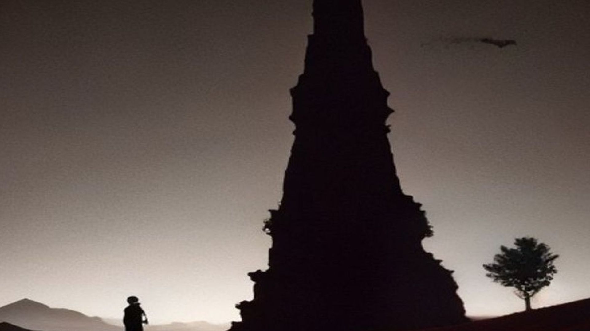 Cinco viajeros caminando en fila por una llanura vacía hacia una torre oscura lejana al atardecer