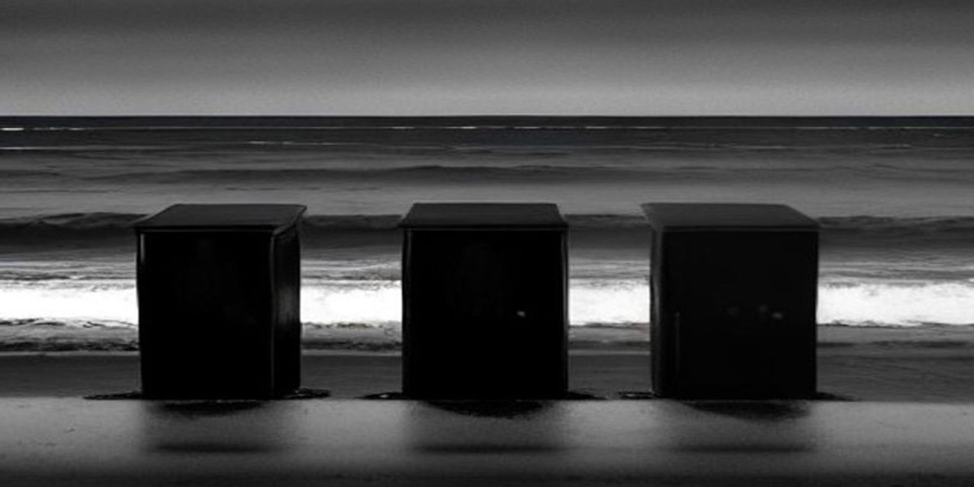 Tres puertas de madera en pie sobre una playa desierta al atardecer, frente a un mar gris