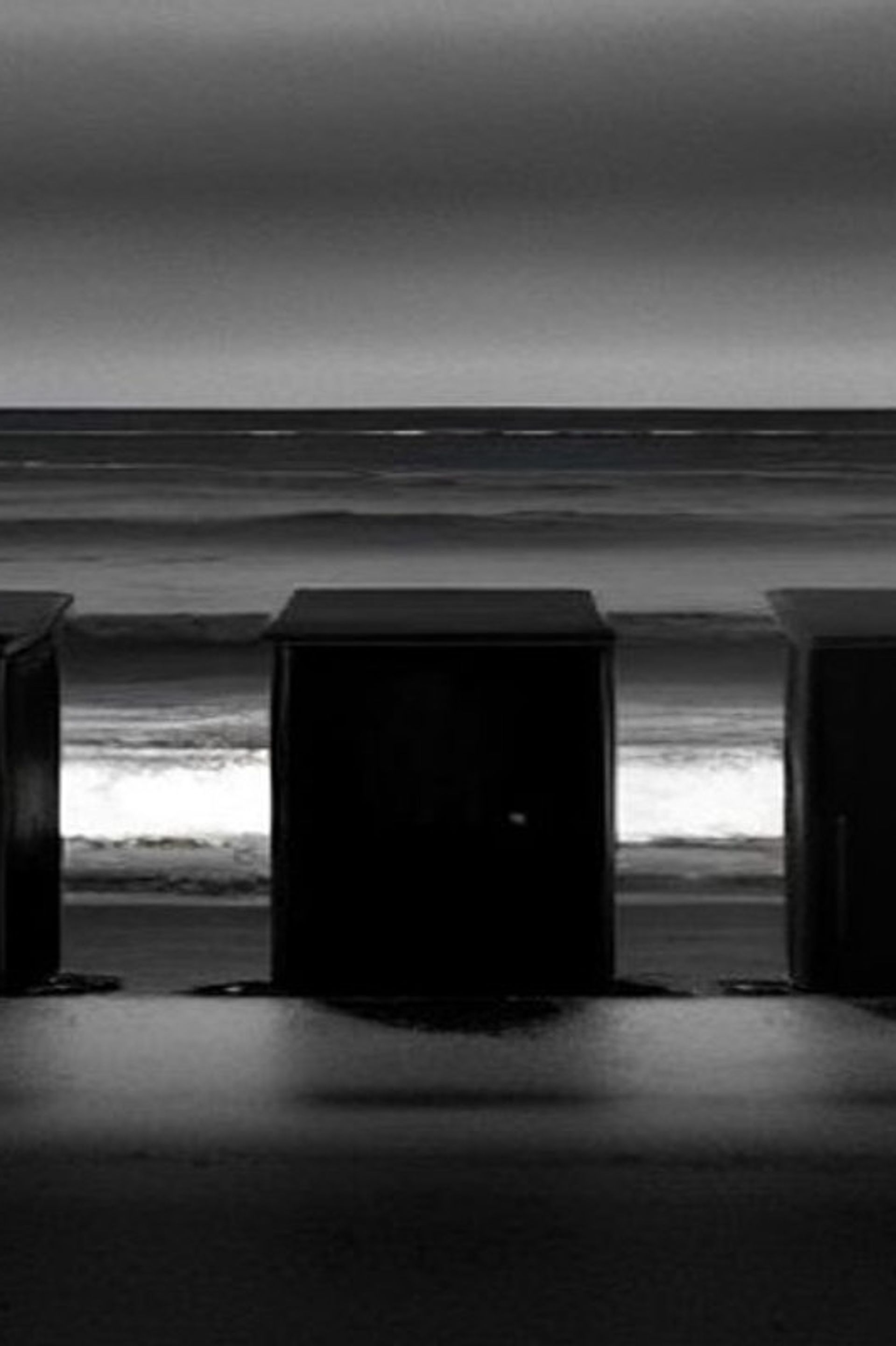 Tres puertas de madera en pie sobre una playa desierta al atardecer, frente a un mar gris