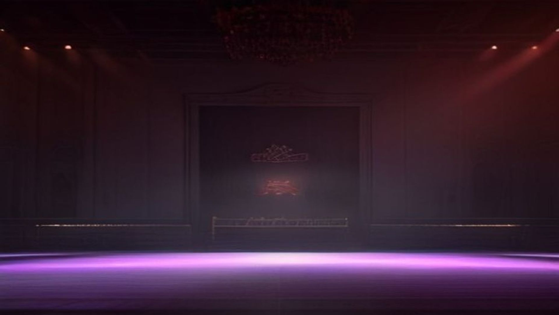 Gimnasio escolar decorado para un baile de graduación, bañado en luz roja, con una corona sobre una silla en el escenario vacío