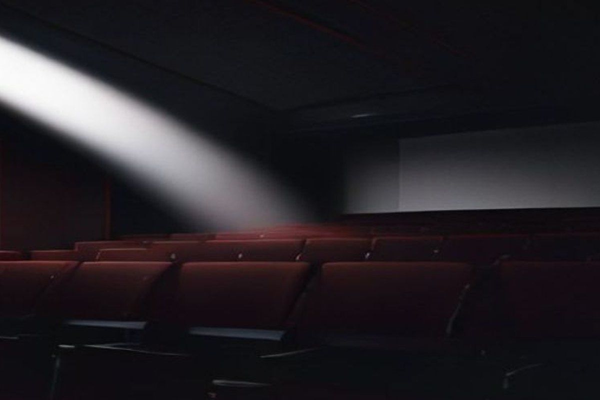 Sala de cine vacía con el haz del proyector iluminando una pantalla con un campo dorado