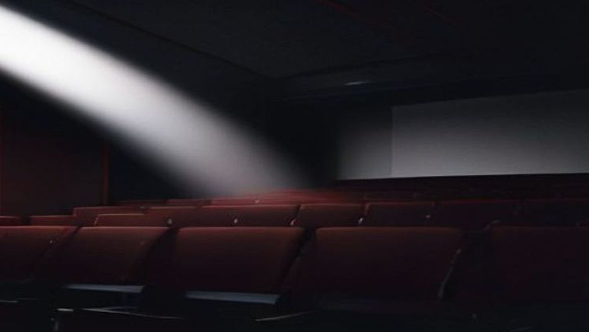 Sala de cine vacía con el haz del proyector iluminando una pantalla con un campo dorado