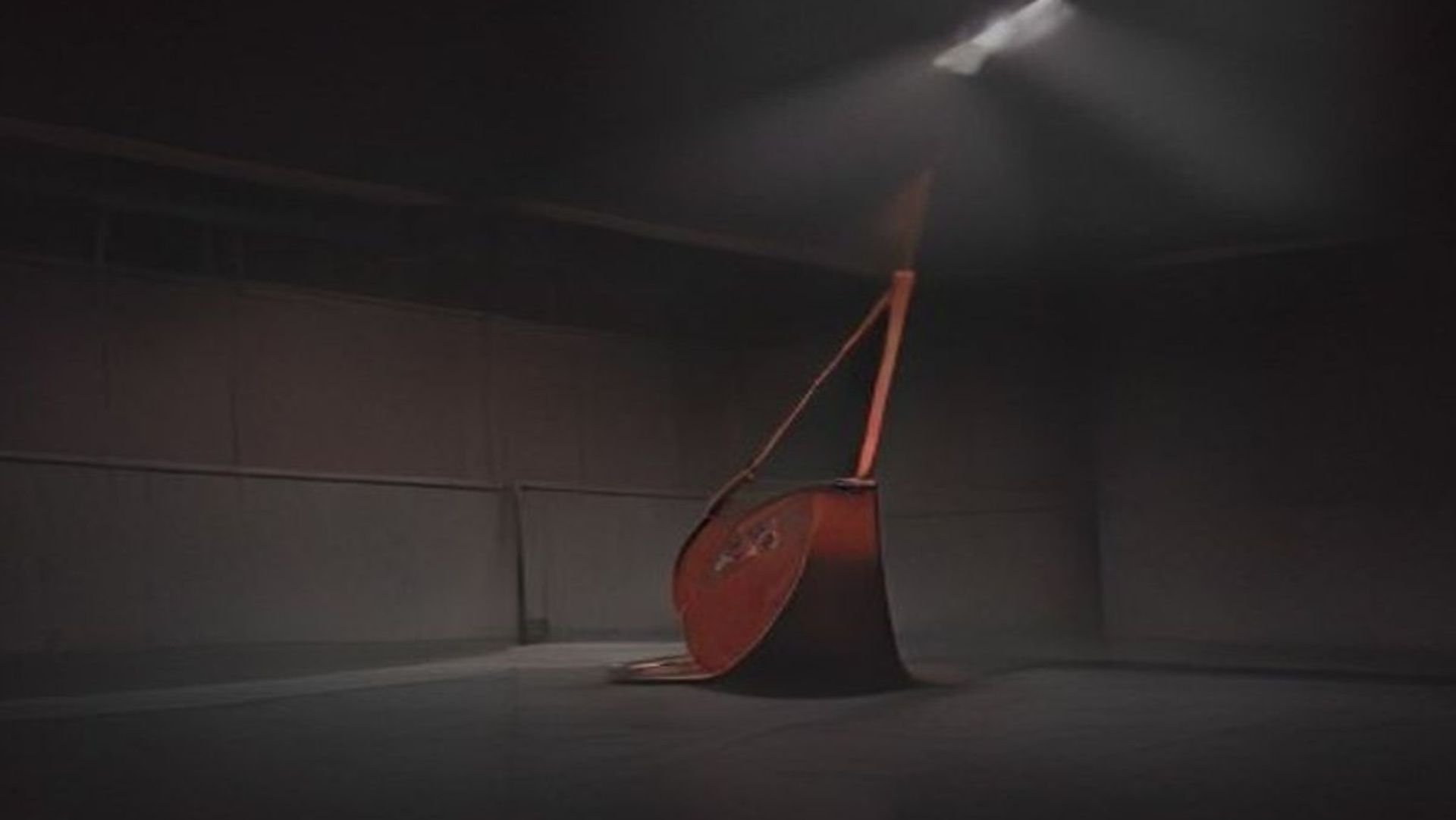 Gimnasio escolar vacío de noche, decorado para un baile de graduación, con un cubo metálico volcado sobre el escenario bajo un foco duro