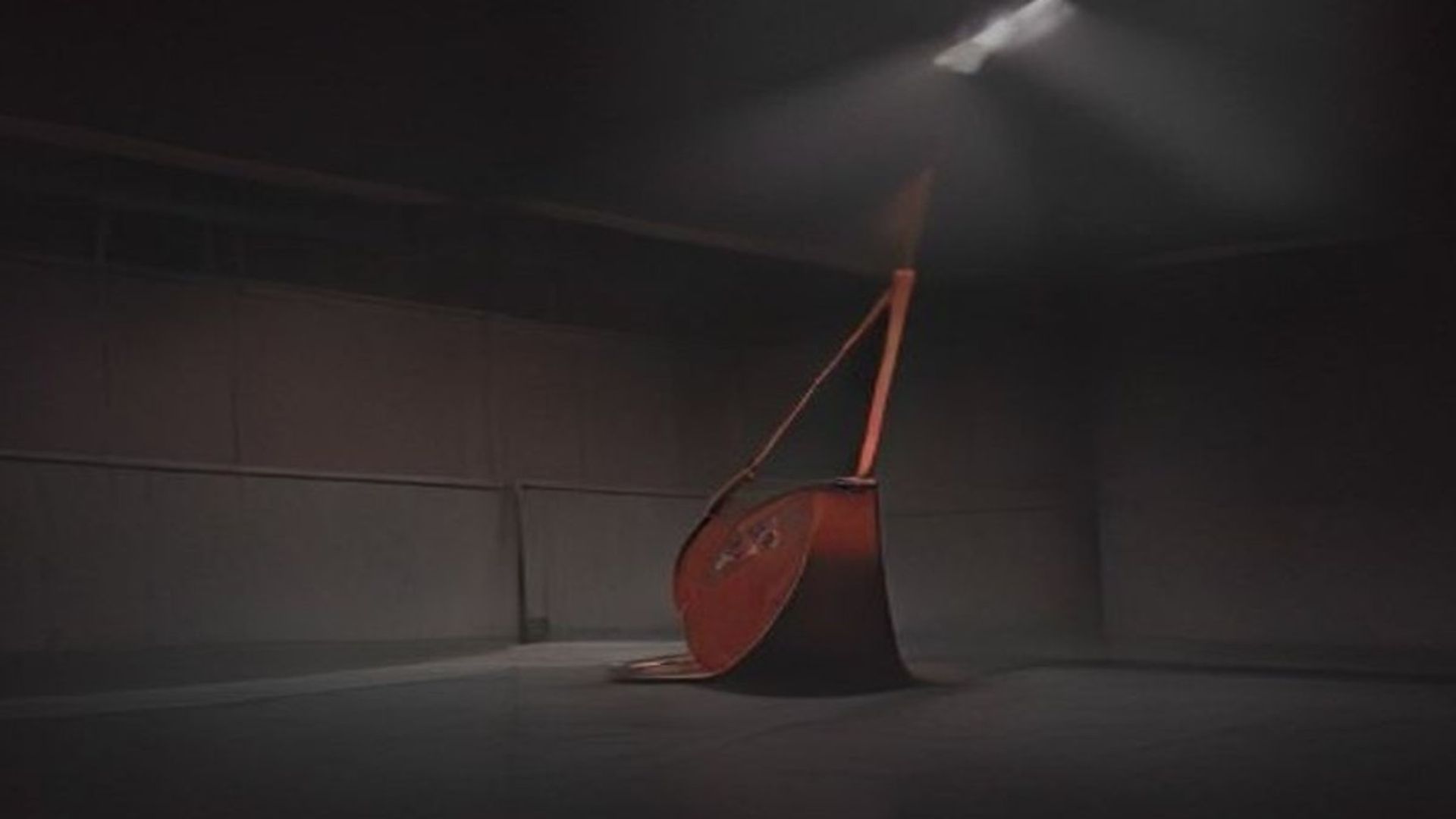 Gimnasio escolar vacío de noche, decorado para un baile de graduación, con un cubo metálico volcado sobre el escenario bajo un foco duro