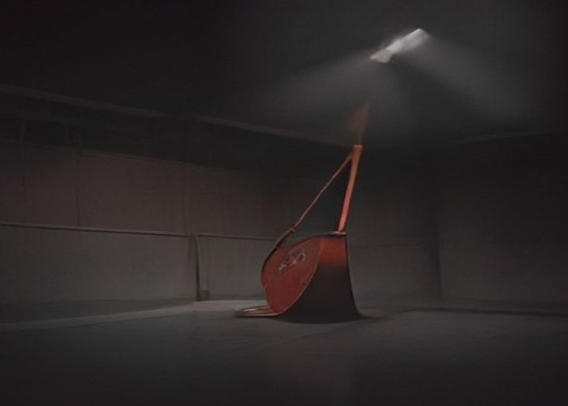 Gimnasio escolar vacío de noche, decorado para un baile de graduación, con un cubo metálico volcado sobre el escenario bajo un foco duro