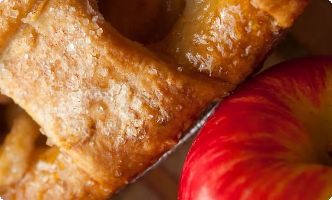 An apple pie in a tin with a bright red apple leaning on it.