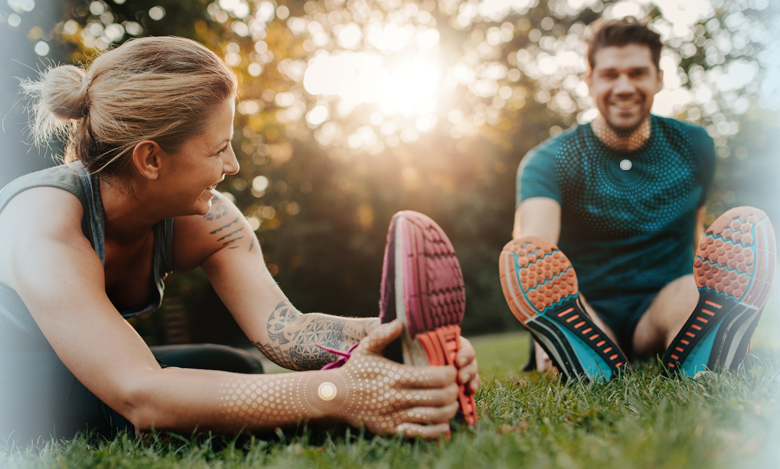 A woman and a man in athletic clothing stretching on grass