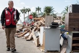 Relief worker in red vest walking past hurricane debris
