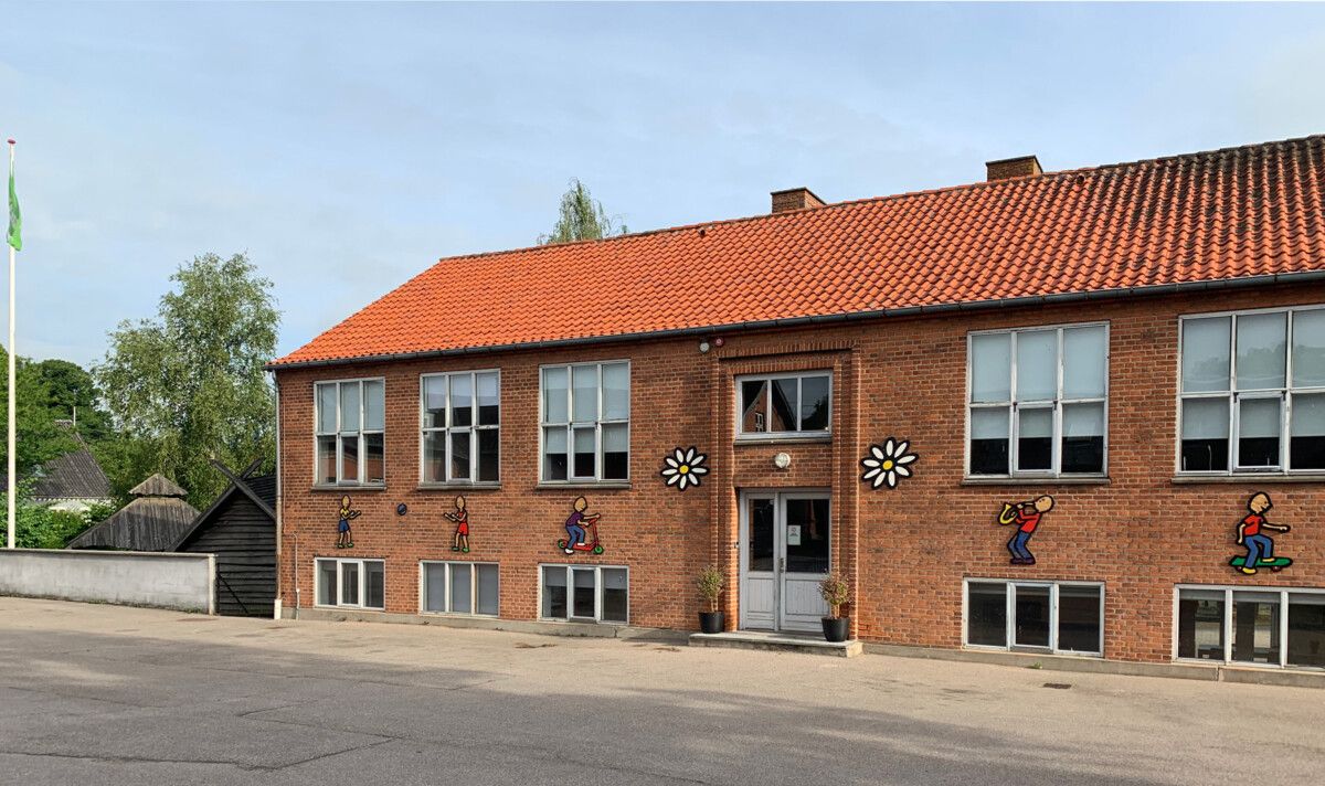 Skolebygning i røde mursten med farverige figurer malet på facaden