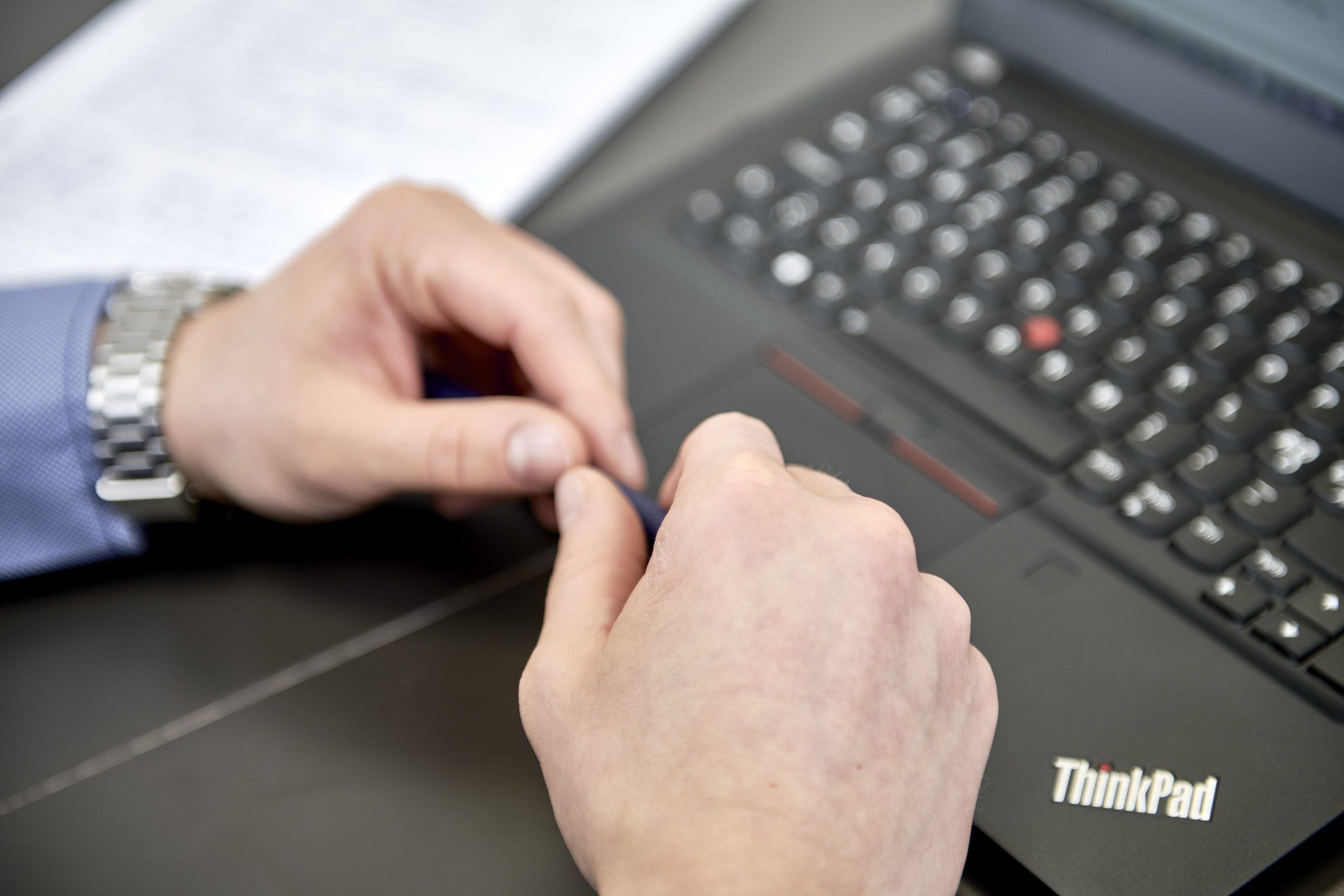 Nærbillede af to hænder ved en ThinkPad-laptop og et stykke papir under et møde hos NTD