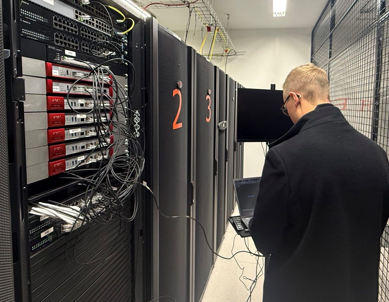 Tekniker med laptop foran åbne serverracks i et datacenter