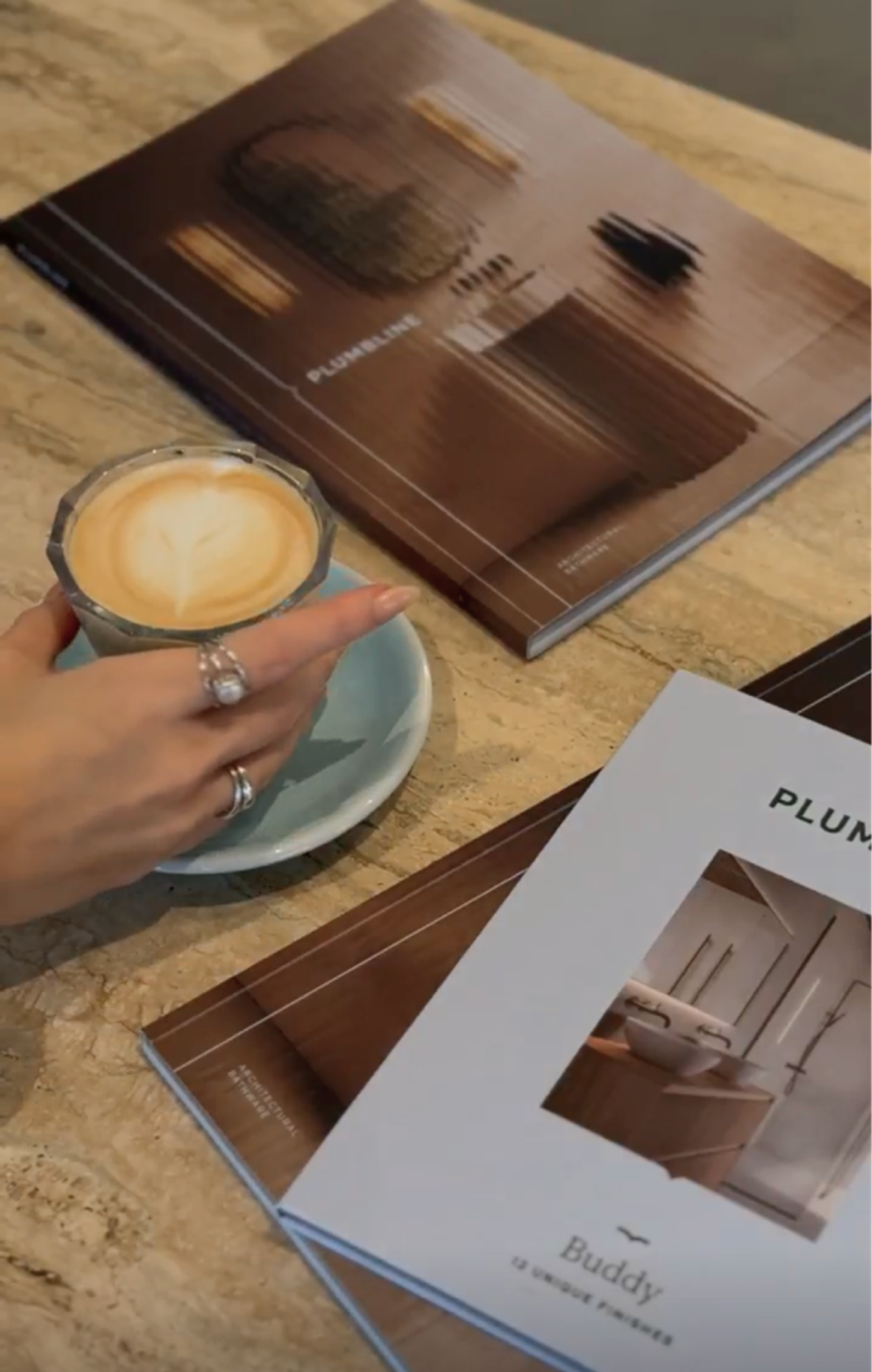 A hand holding a coffee over two Plumbline catalogues on marble