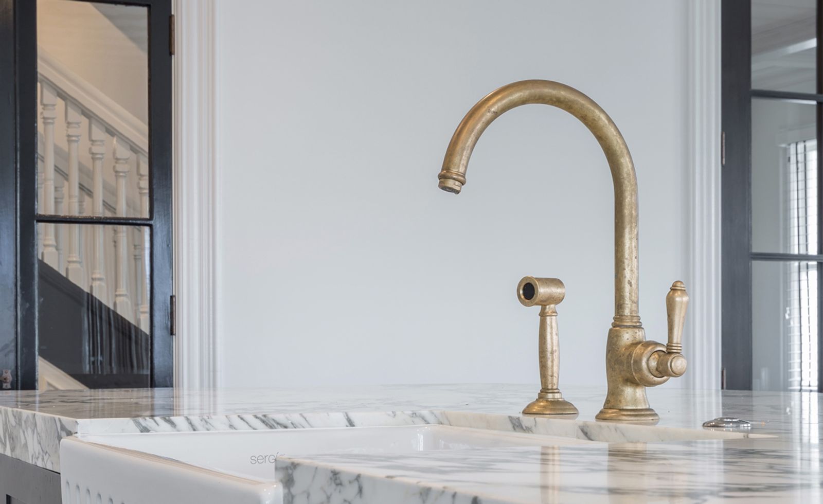 Aged brass kitchen mixer and spray on a marble benchtop above a white butler sink