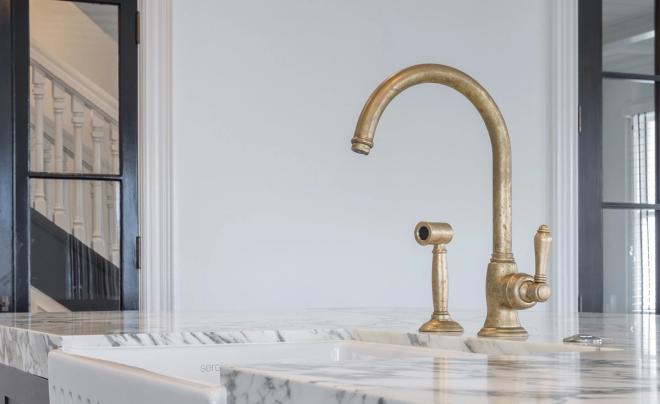 Aged brass kitchen mixer and spray on a marble benchtop above a white butler sink