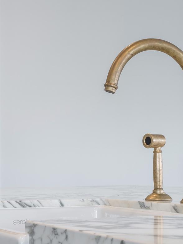 Aged brass kitchen mixer and spray on a marble benchtop above a white butler sink