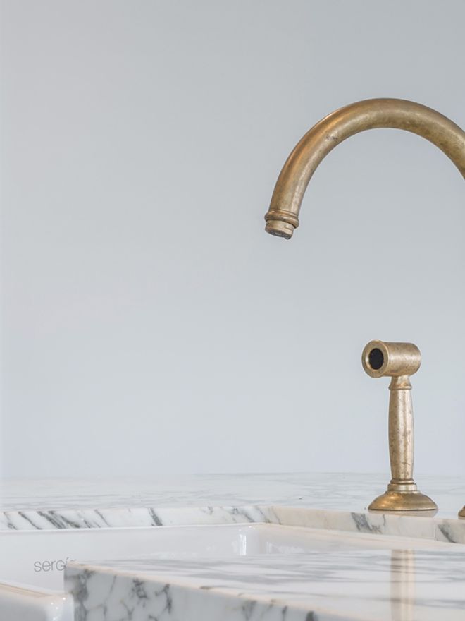 Aged brass kitchen mixer and spray on a marble benchtop above a white butler sink