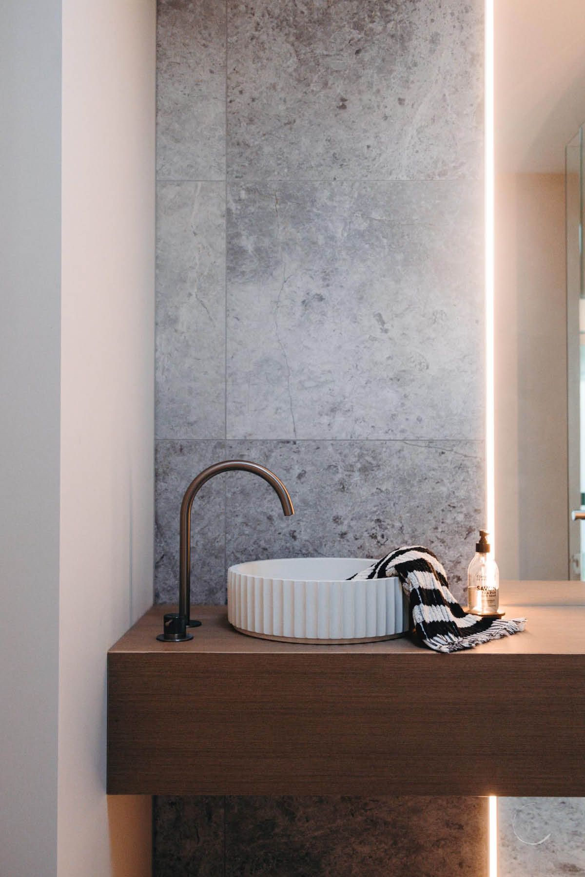 Fluted basin with bronze tapware on stone wall