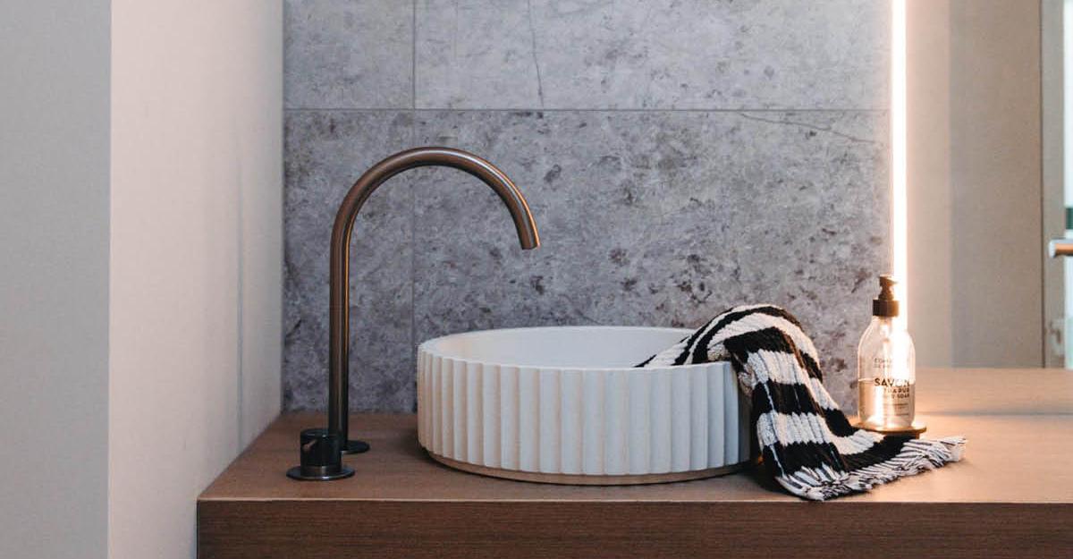 Fluted basin with bronze tapware on stone wall