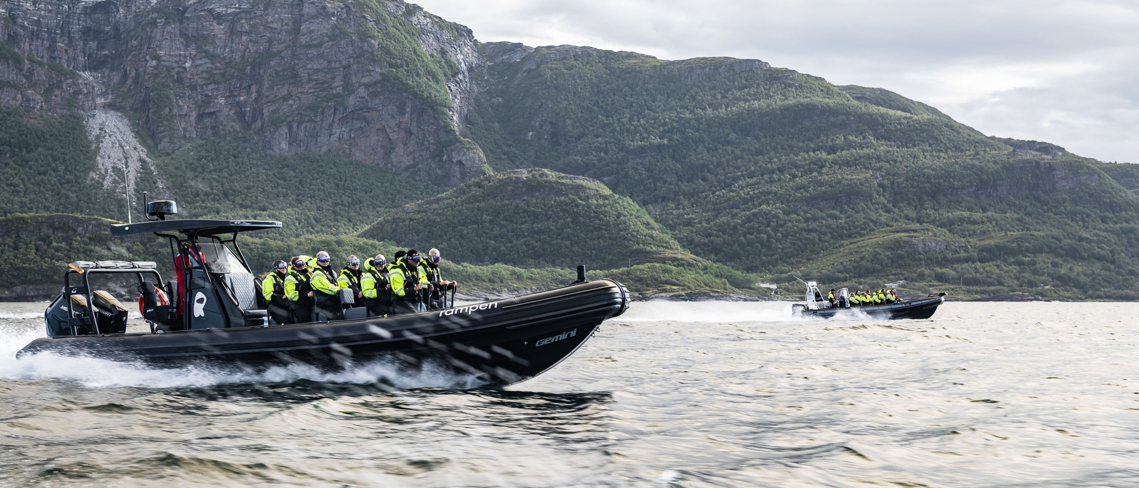 Test Title To RIB båter kjører på vannet i fart, i bakgrunnen ser man fjell og