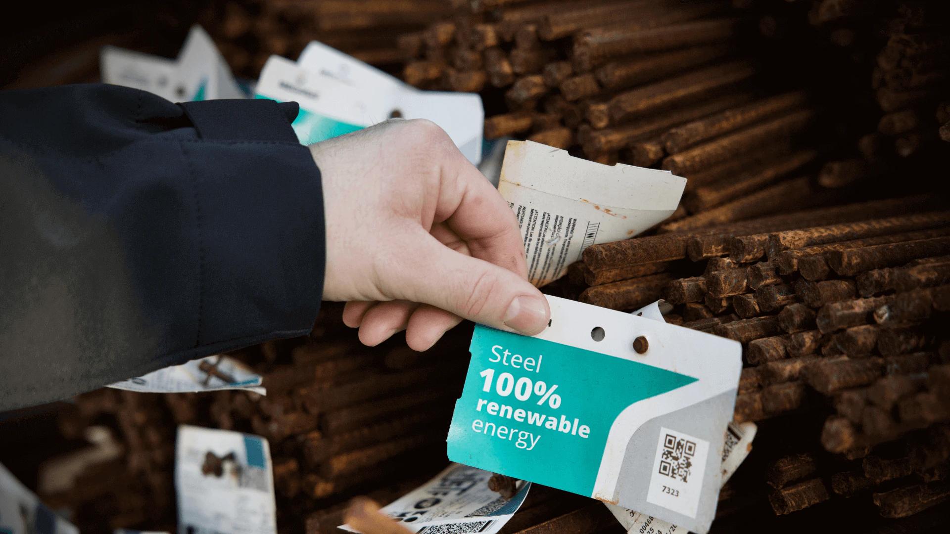 Hand holding a “Steel 100% renewable energy” tag on bundles of steel bars