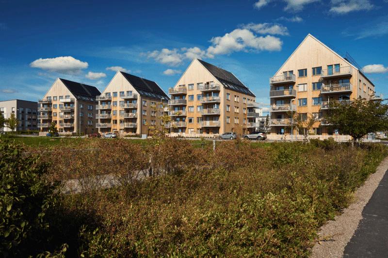 Four apartment buildings with solar panels on their pitched roofs behind a meadow, a Bonava project