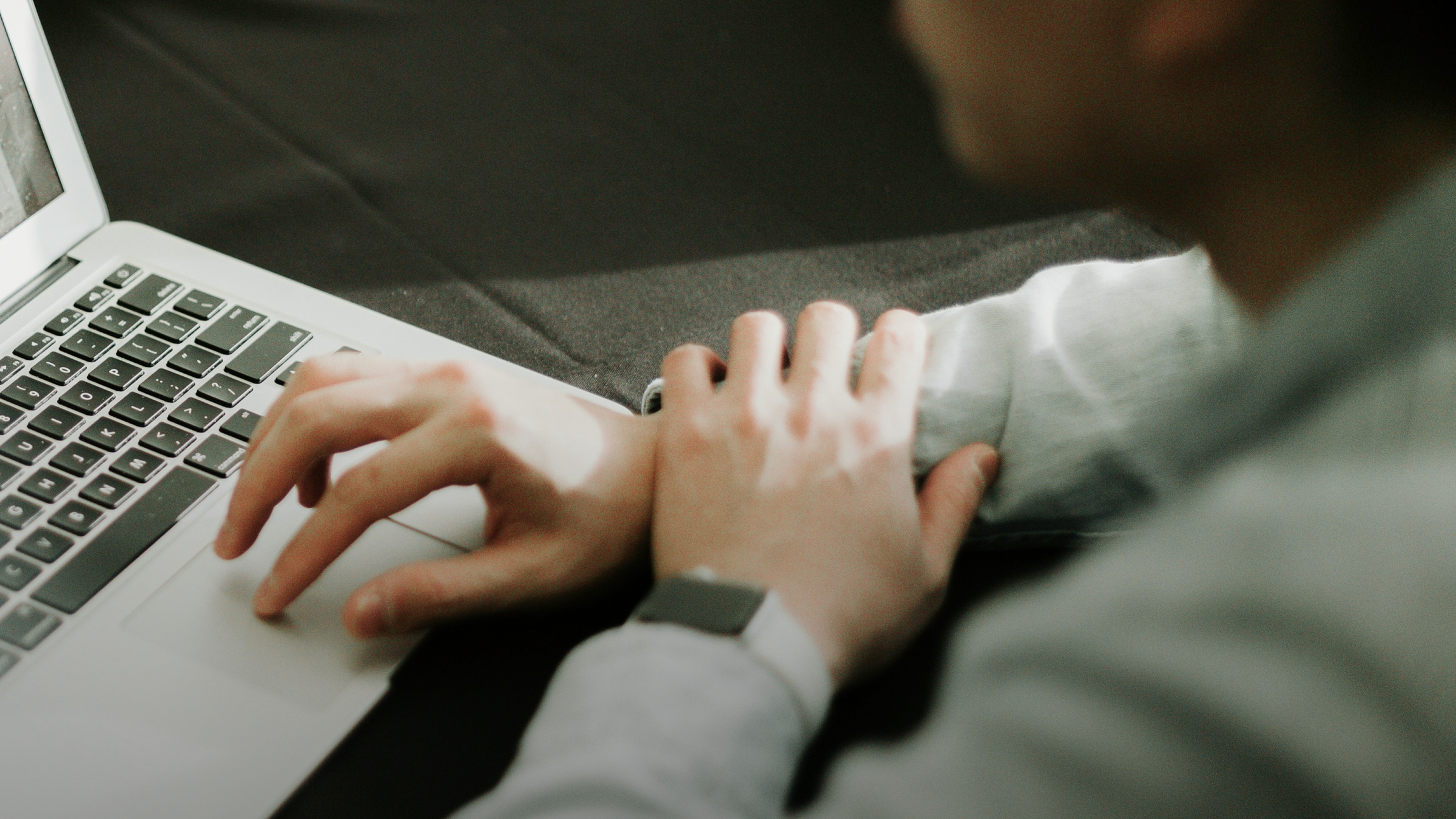 Overhead view of a person's hands using a laptop, one on the trackpad, wearing a smartwatch.