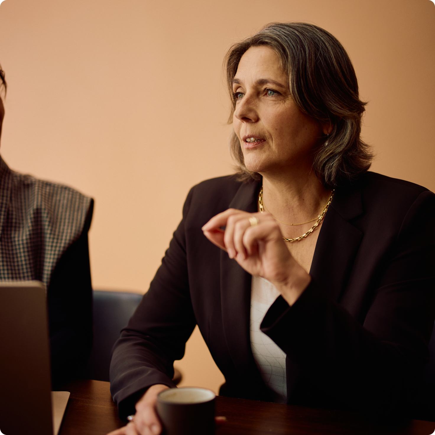 A lawyer in a dark blazer speaks with a colleague across a meeting table.