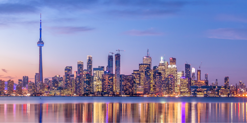 Toronto skyline with CN Tower at dusk, reflected in water.