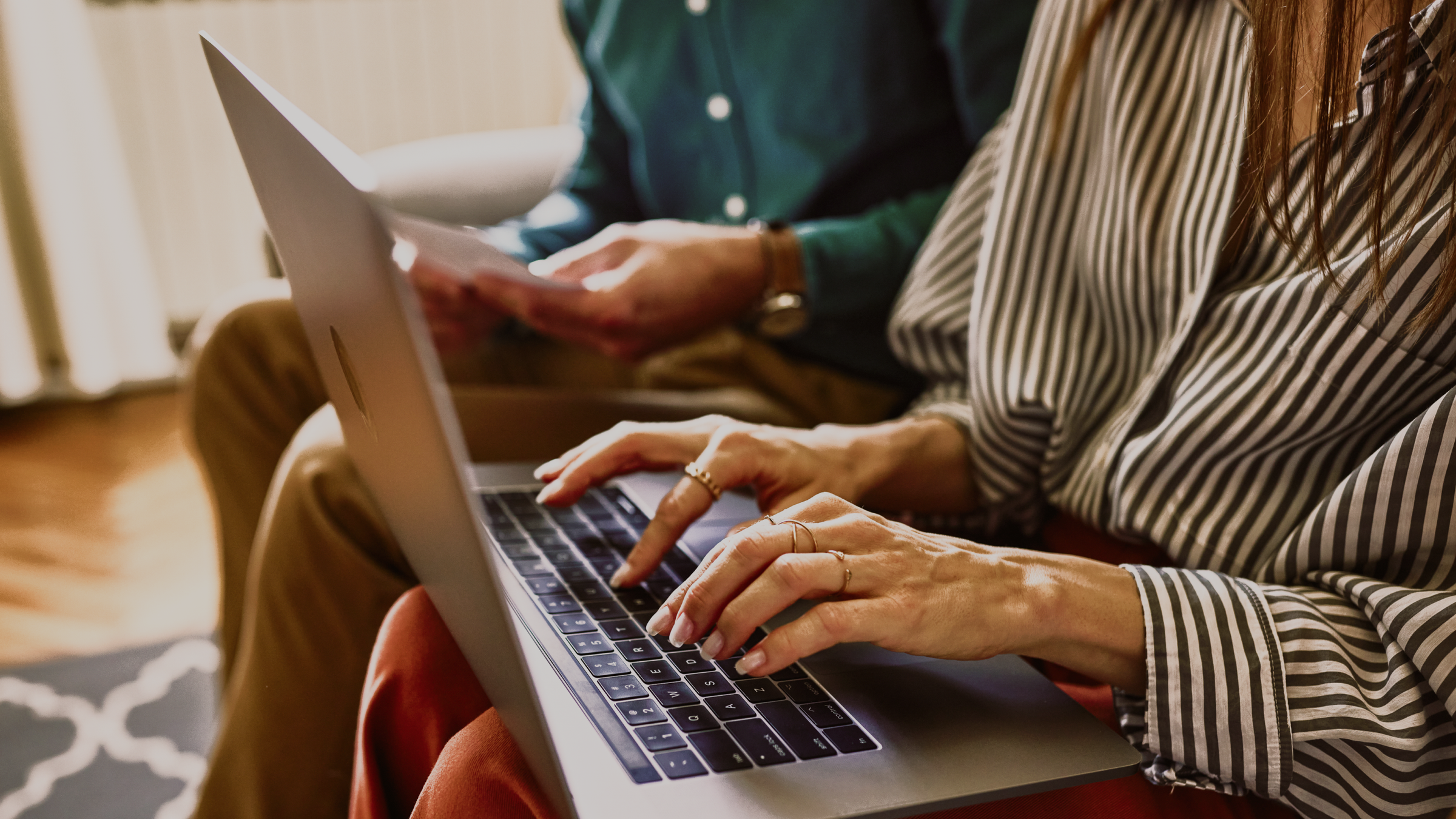Woman typing on a laptop, man with documents in background.
