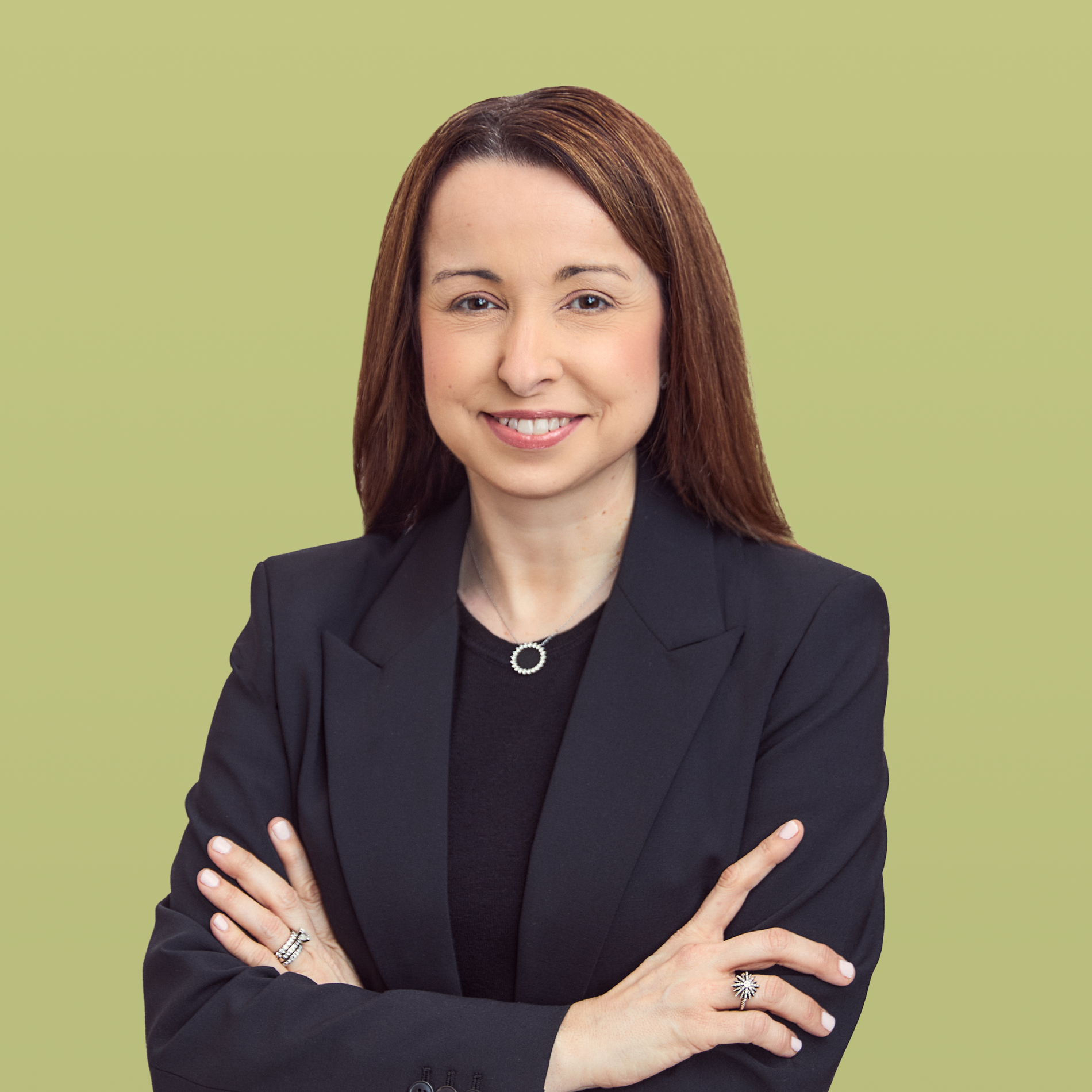 Headshot of a smiling woman with brown hair, wearing a black blazer with arms crossed.