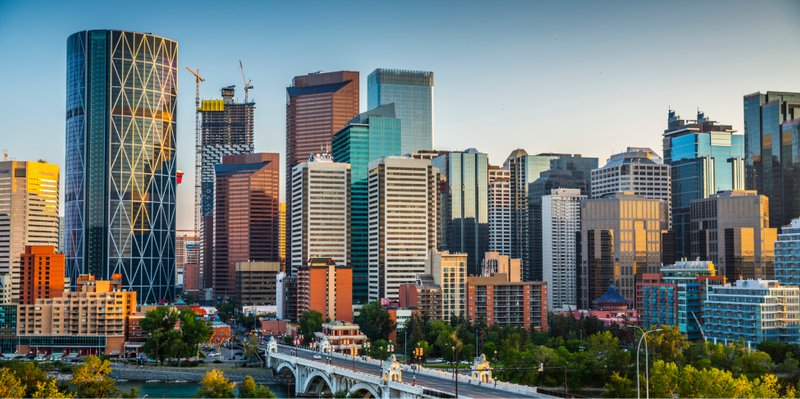 Modern city skyline with numerous skyscrapers, a bridge spanning a river, and green trees.