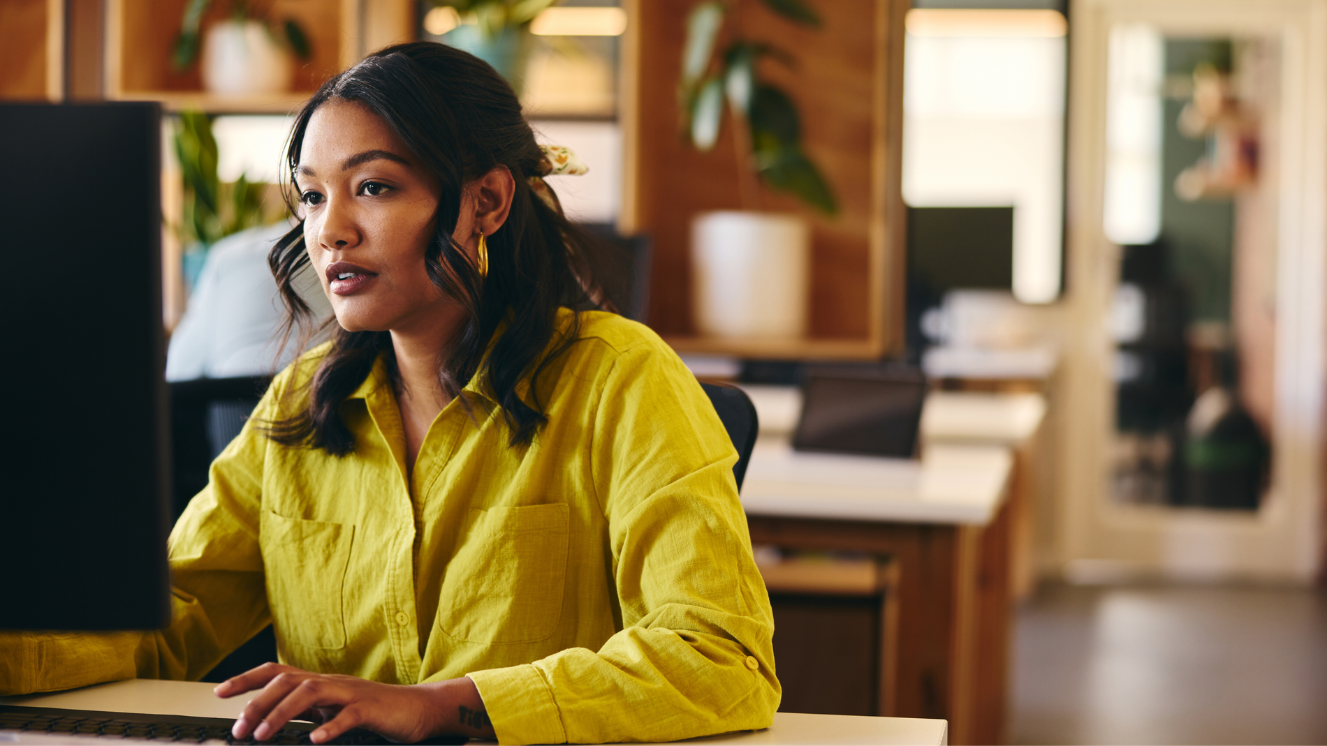 A young woman in a yellow shirt works on a computer in an office.