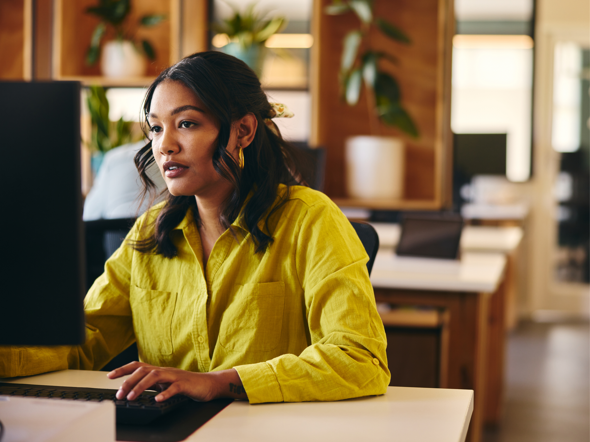 A professional in a yellow shirt working at a desktop computer in an office.