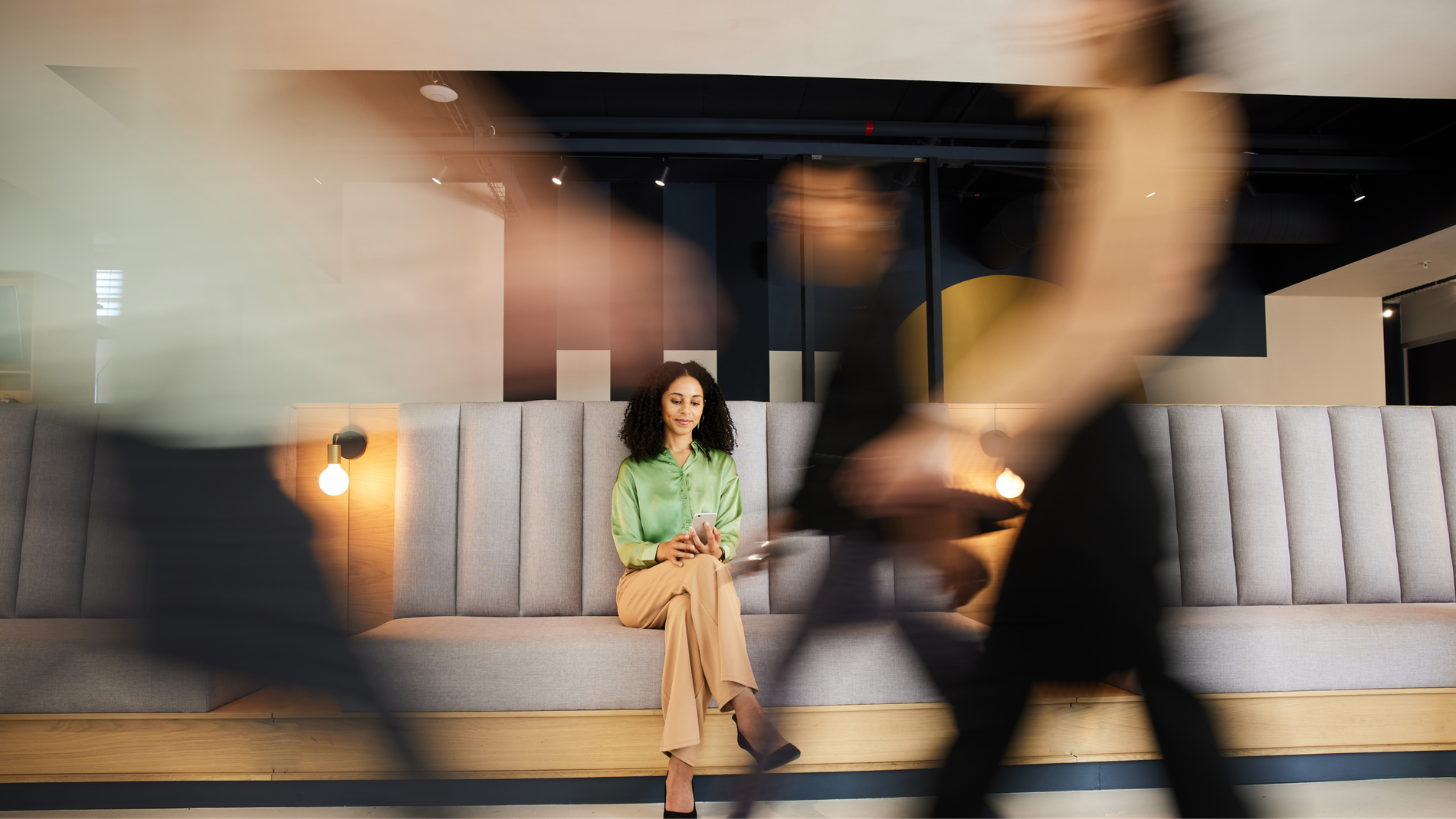 A woman sits calmly on a bench while blurred figures of people walk past.