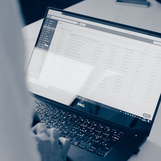 Hands typing on a Dell laptop displaying a data list.