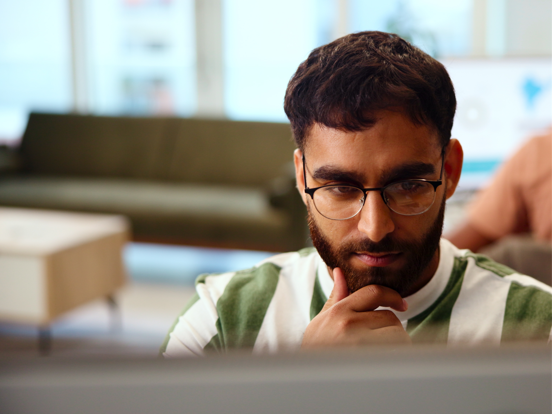 Man with beard and glasses in striped shirt, looking intently down, hand on chin.