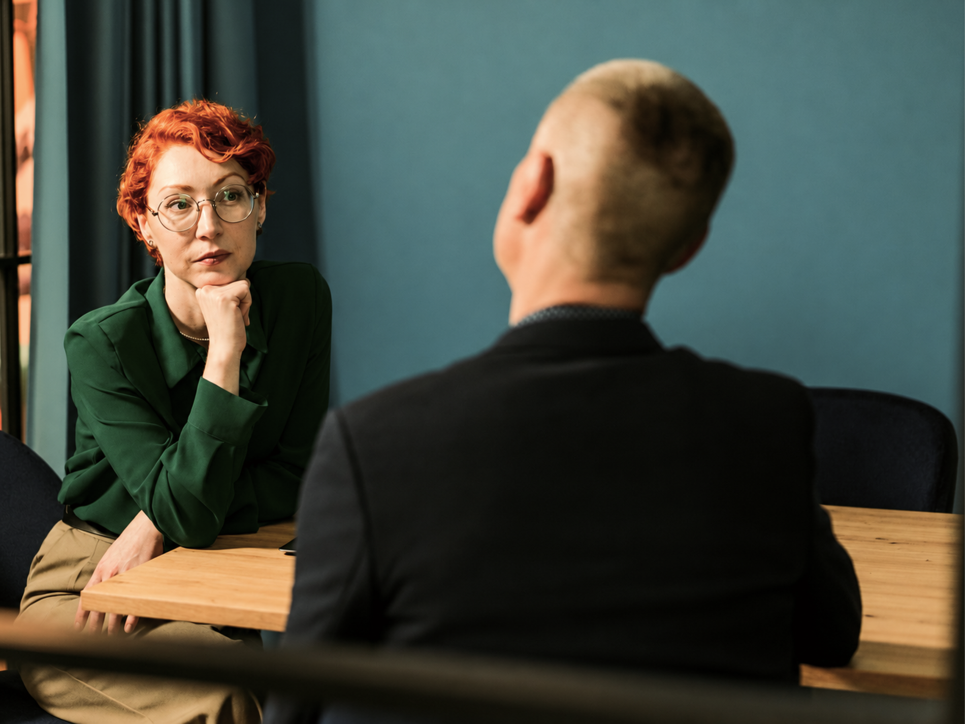 A professional in a green blouse listening to a colleague across a meeting table.