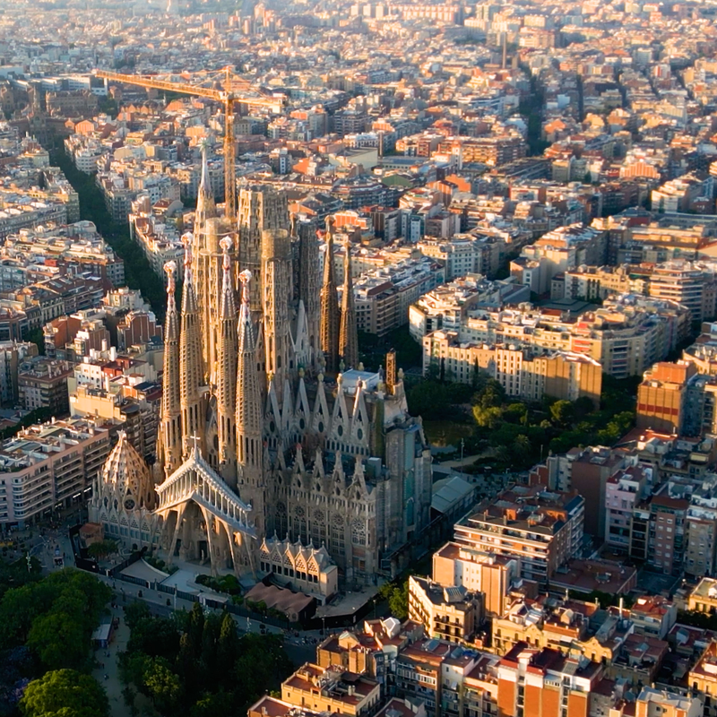 Aerial view of Barcelona's Sagrada Familia with a construction crane, surrounded by the city's grid under warm light.