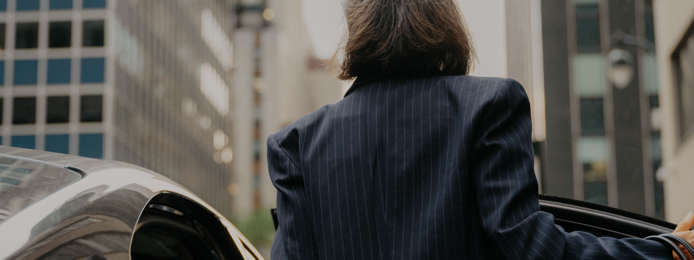 Person in a pinstripe jacket entering a car in a city.
