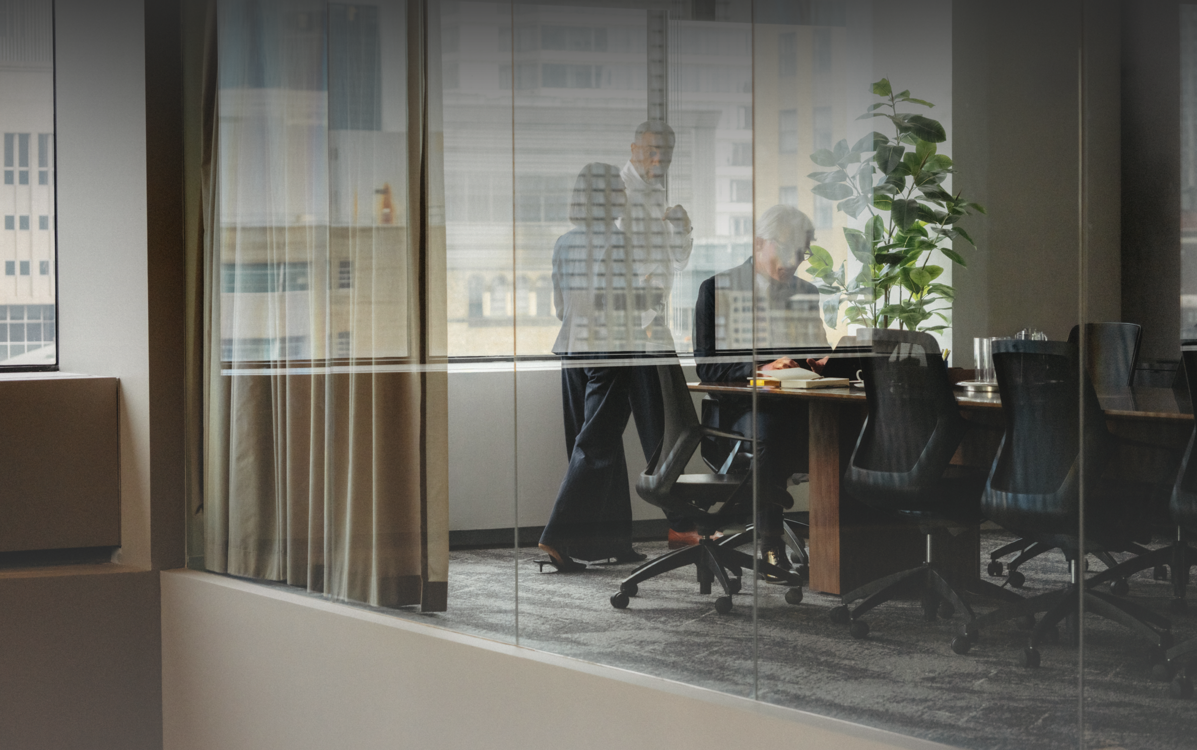 Three people meeting in a glass-walled conference room.