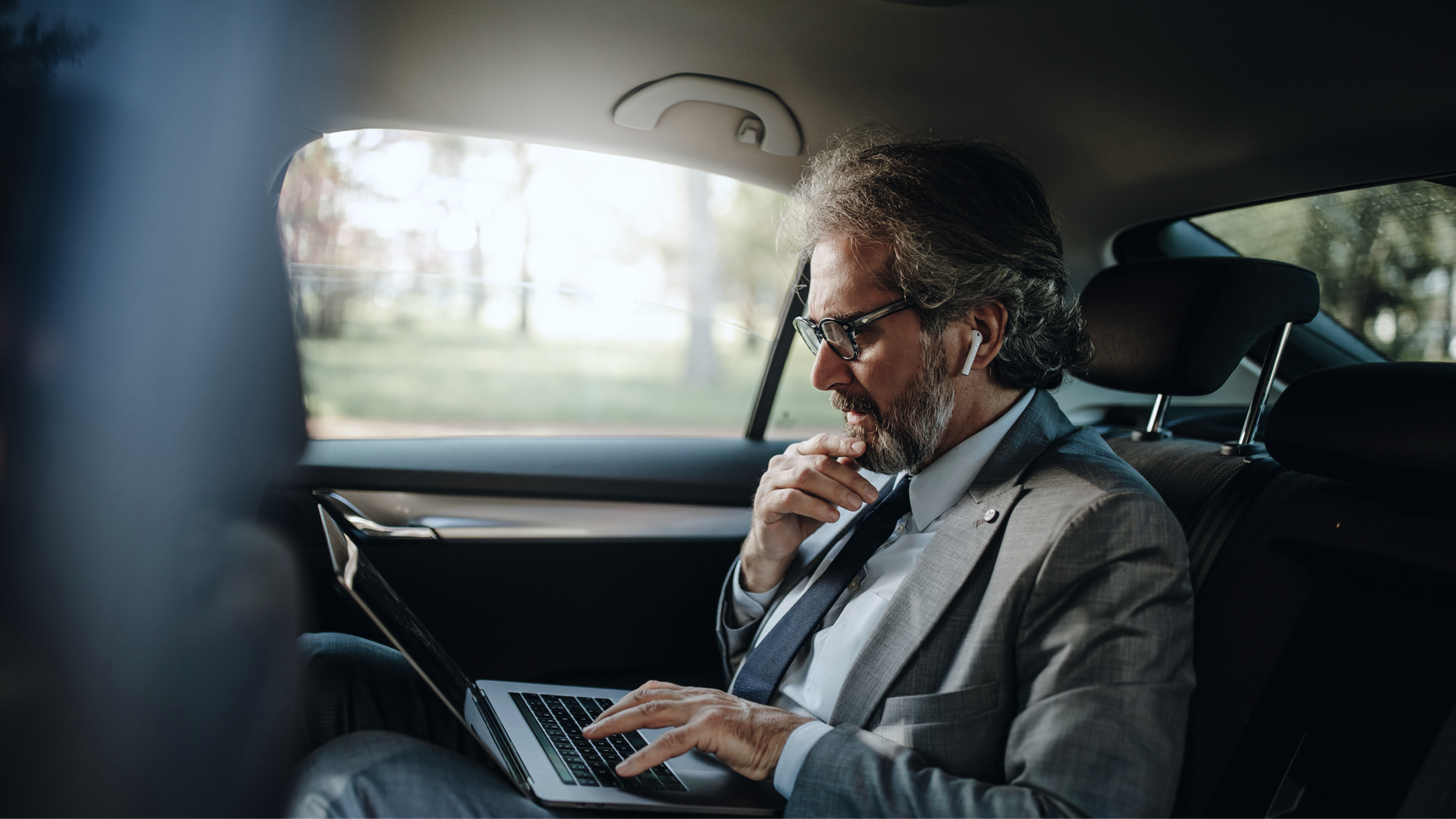Businessman working on laptop in car back seat.